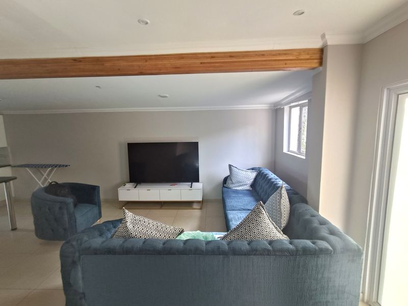 A comfortable living room featuring tiled flooring, recessed downlighting, and a decorative exposed timber beam, creating a bright and open atmosphere.