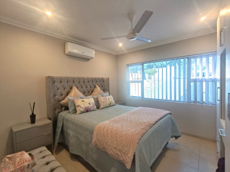 A well-maintained bedroom featuring tiled flooring, a ceiling fan, a split-system air conditioner, and built-in cupboards with ample natural light.