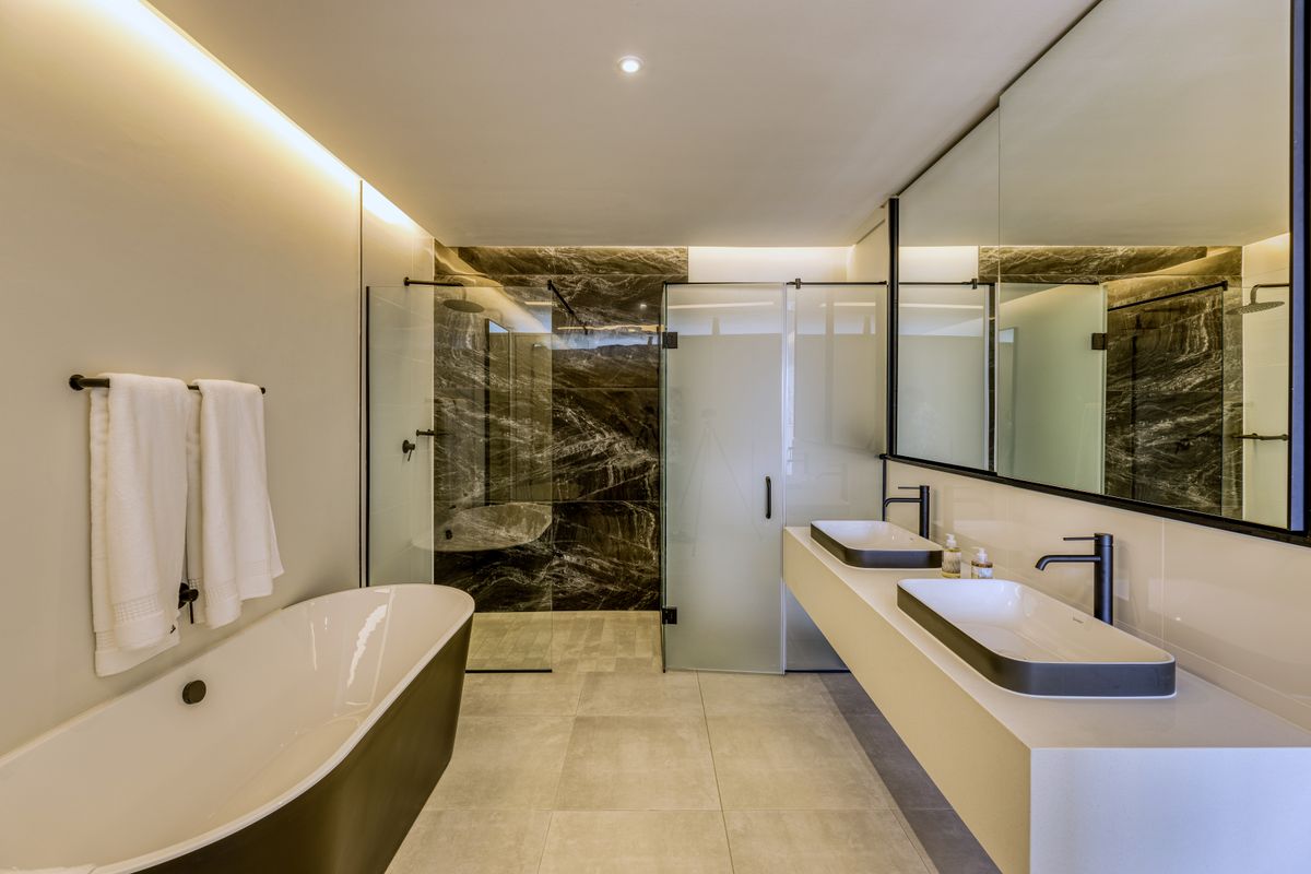 Modern bathroom featuring a freestanding bathtub, a spacious walk-in glass shower with dark marble-effect tiling, and a sleek double vanity with matte black fixtures.