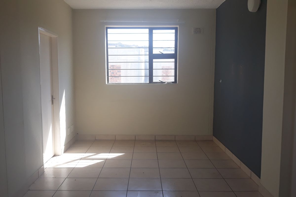 An empty bedroom featuring tiled flooring, a window with security bars, and a dark accent wall, offering a blank canvas for personalization.