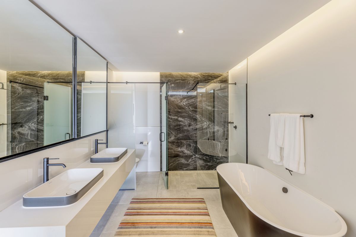 Modern bathroom featuring a double vanity with vessel sinks, a freestanding bathtub, and a spacious walk-in shower with dark marble-style wall tiling.