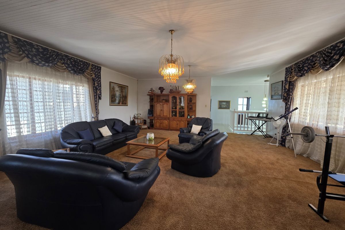 Spacious living room featuring timber tongue and groove ceilings, ornate chandeliers, and carpet flooring, offering a traditional layout with an open transition to the hallway.