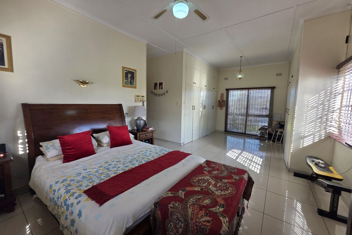 Spacious bedroom featuring tiled flooring, built-in cupboards, a ceiling fan, and a sliding door with venetian blinds providing natural light.