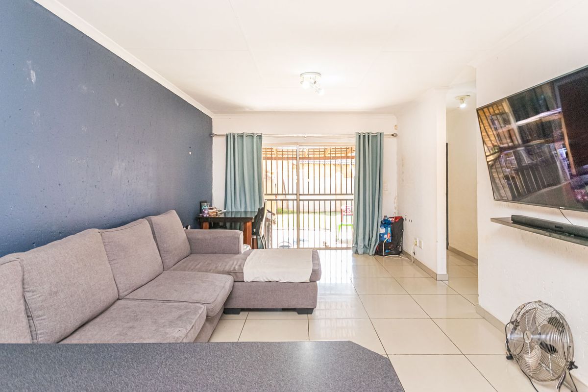 A living room featuring tiled flooring, a sliding glass door with security gate, and a feature wall, providing access to the outdoor area.