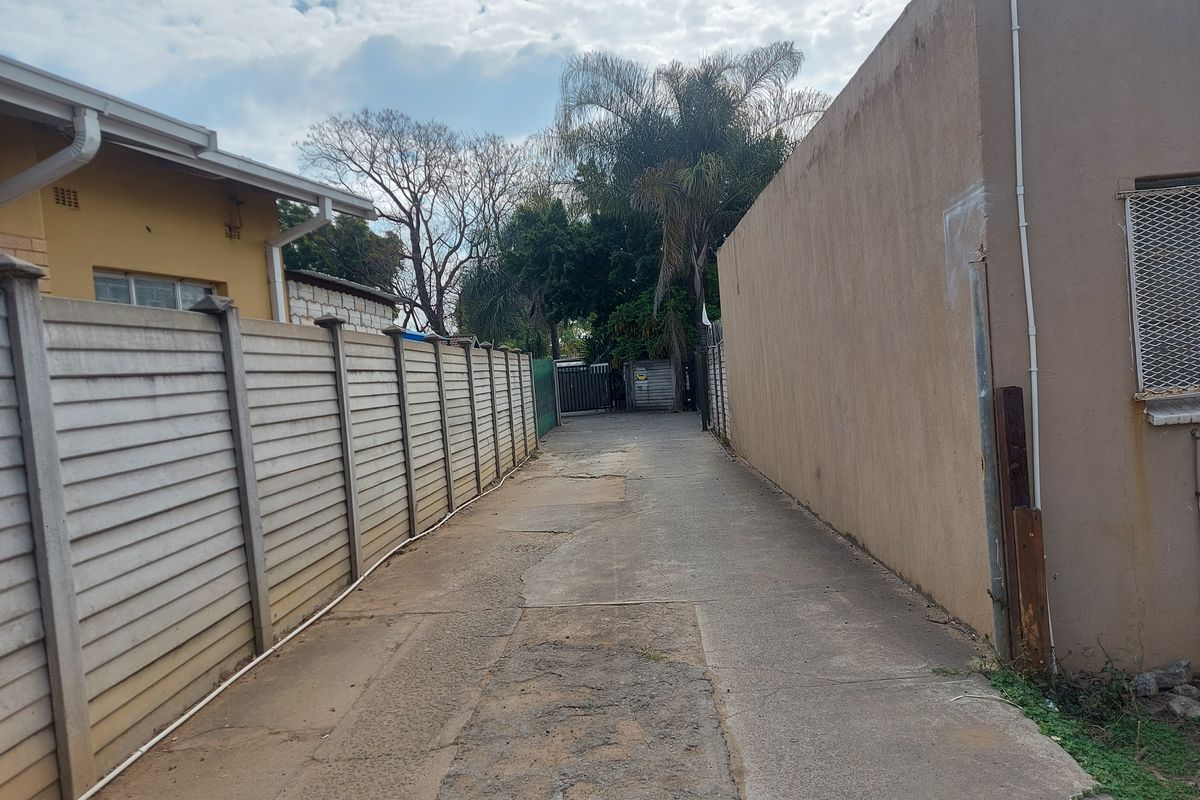 A narrow concrete driveway leading to the rear of the property, enclosed by a precast concrete boundary wall and adjacent building structure.