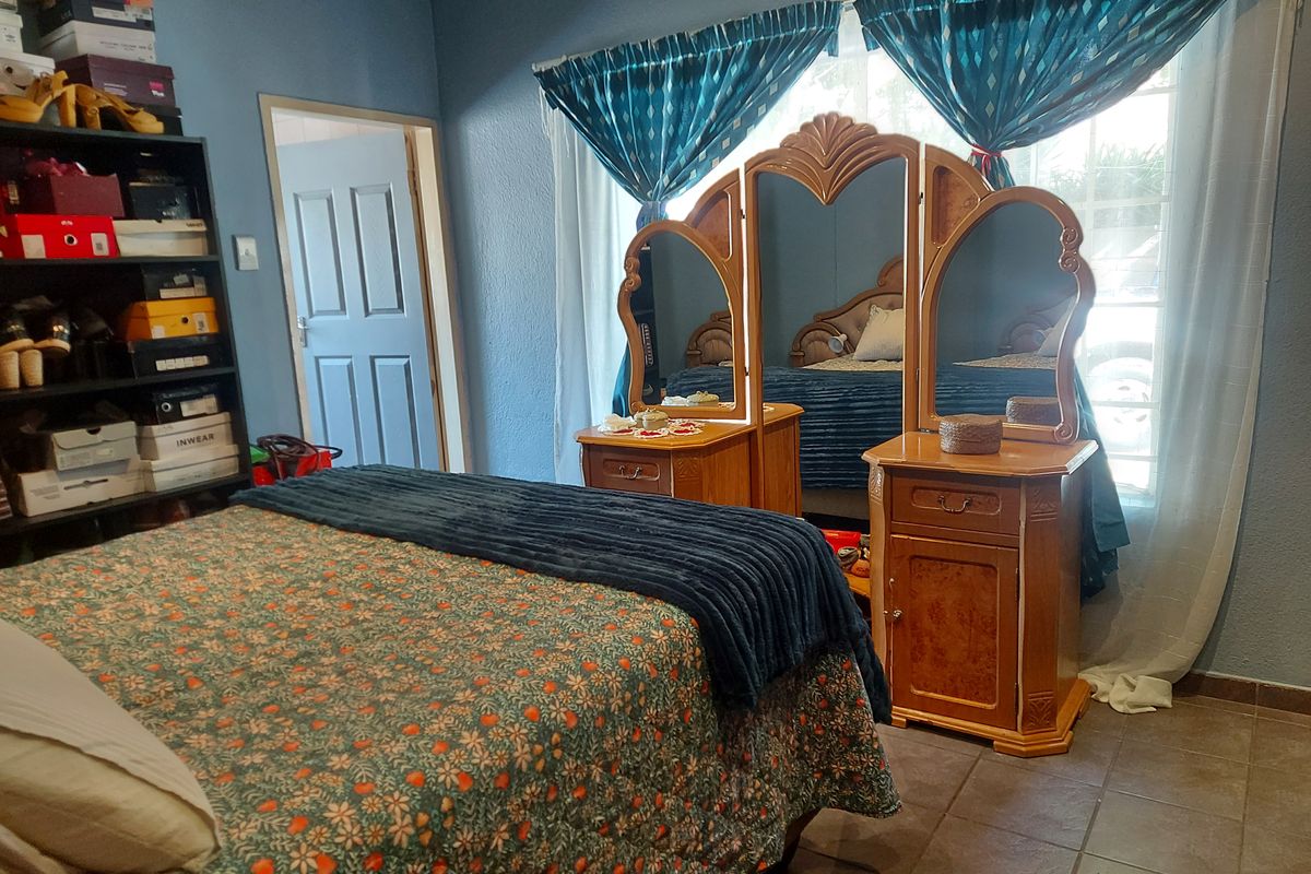 A bedroom featuring tiled flooring and a standard interior door, with natural light provided by a window dressed with curtains.
