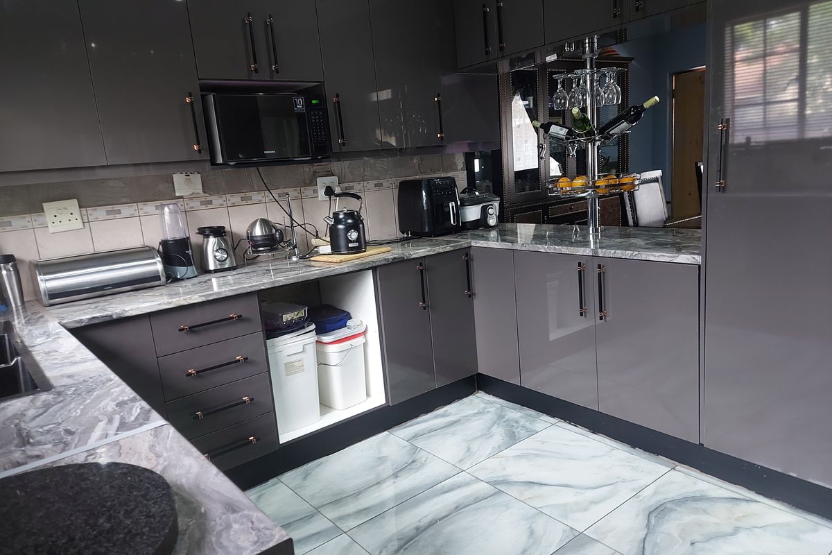 Modern kitchen featuring high-gloss cabinetry, marble-effect countertops, tiled flooring, and a built-in microwave.