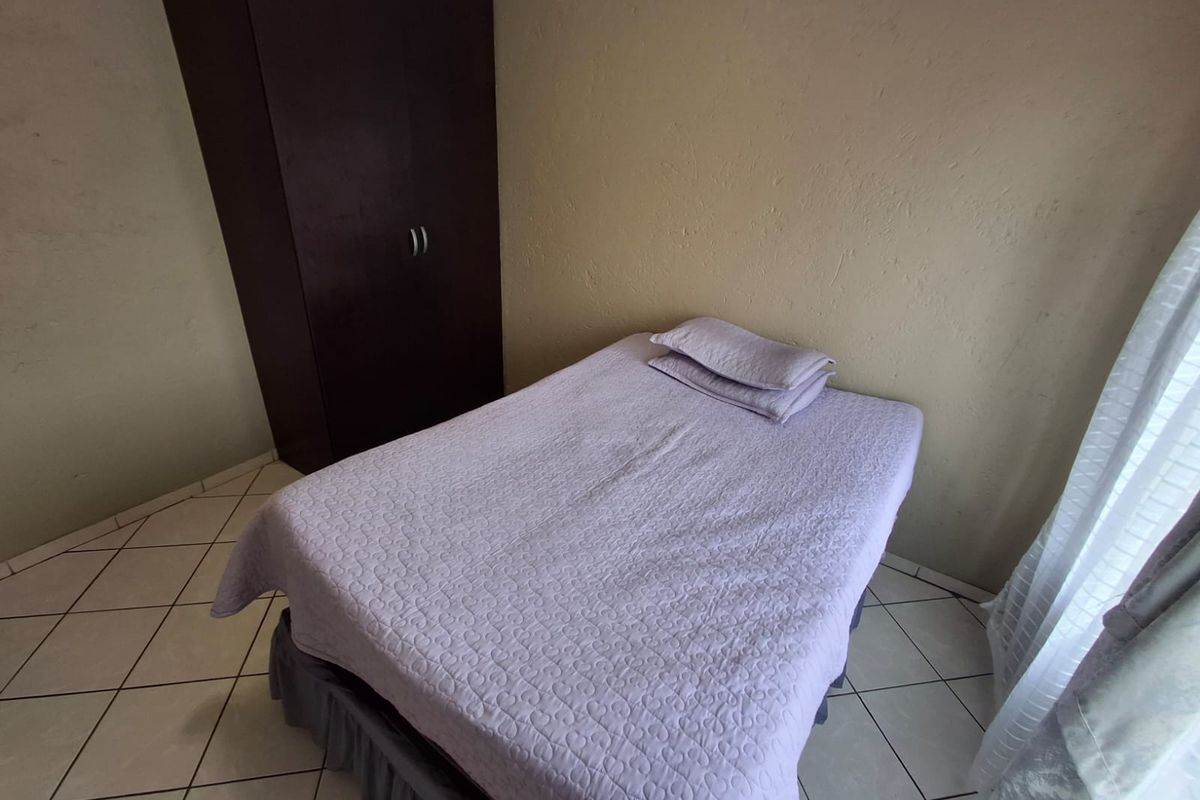 A compact bedroom featuring tiled flooring and a built-in wardrobe, offering a functional space with neutral wall finishes.