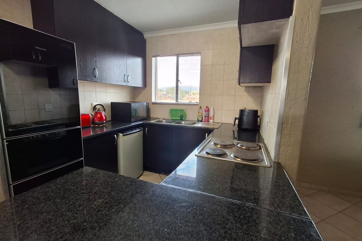 A functional kitchen featuring dark cabinetry, granite countertops, a built-in oven, and an electric hob with a tiled backsplash.