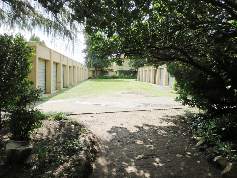 A view of a residential apartment complex featuring a row of multiple garage units with roller shutter doors and a central paved driveway.