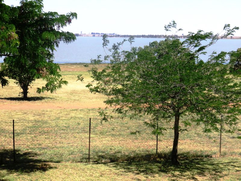 A scenic view overlooking a large body of water with open grassy fields and mature trees in the foreground.