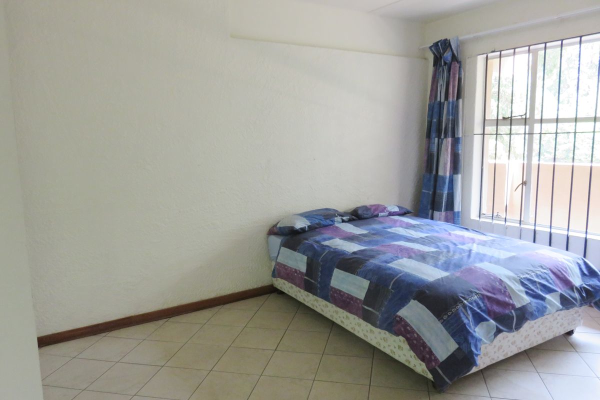 A simple bedroom featuring tiled flooring and a window fitted with security bars, offering a functional space ready for cosmetic updates.