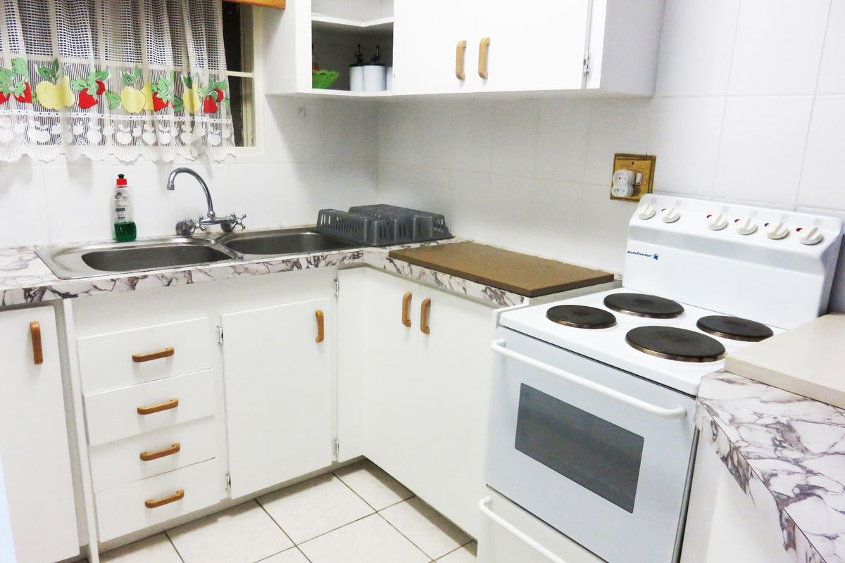 A functional kitchen featuring white cabinetry, laminate countertops, a double basin sink, and a freestanding electric stove with tiled flooring and backsplash.