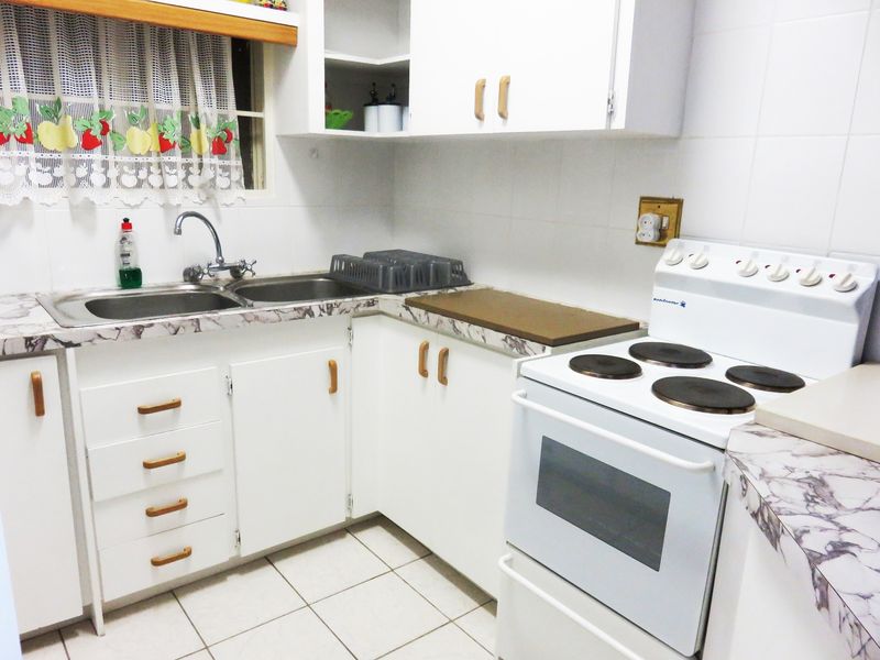 A functional kitchen featuring white cabinetry, laminate countertops, a double basin sink, and a freestanding electric stove with tiled flooring and backsplash.