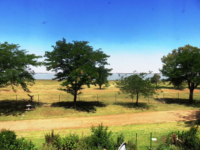 A scenic outdoor view overlooking a large open field with mature trees and a distant body of water.