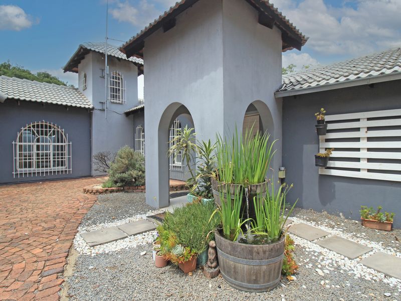 Front entrance area featuring an arched portico, tiled roof, security bars on windows, and a landscaped courtyard with brick paving and gravel.