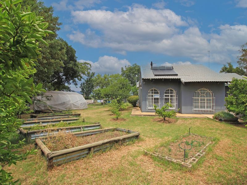 Rear view of the property featuring a garden with raised planting beds, a small greenhouse structure, and a house with a solar water heater.