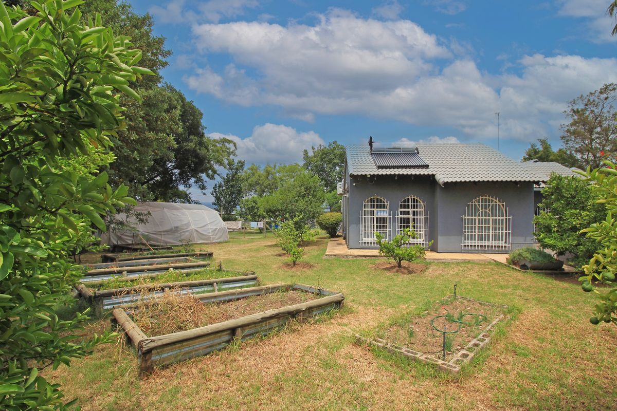 Rear view of the property featuring a garden with raised planting beds, a small greenhouse structure, and a house with a solar water heater.