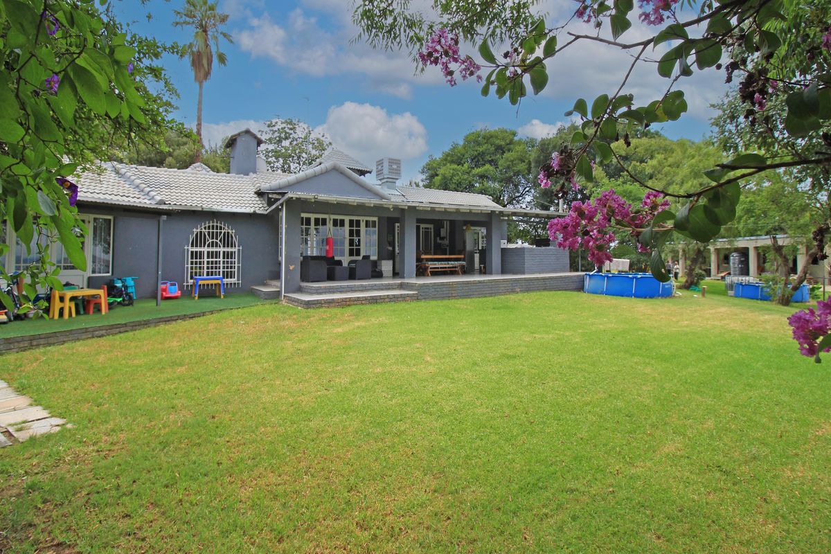 Rear view of the house featuring a spacious lawn, a covered patio area, and a tiled roof structure.