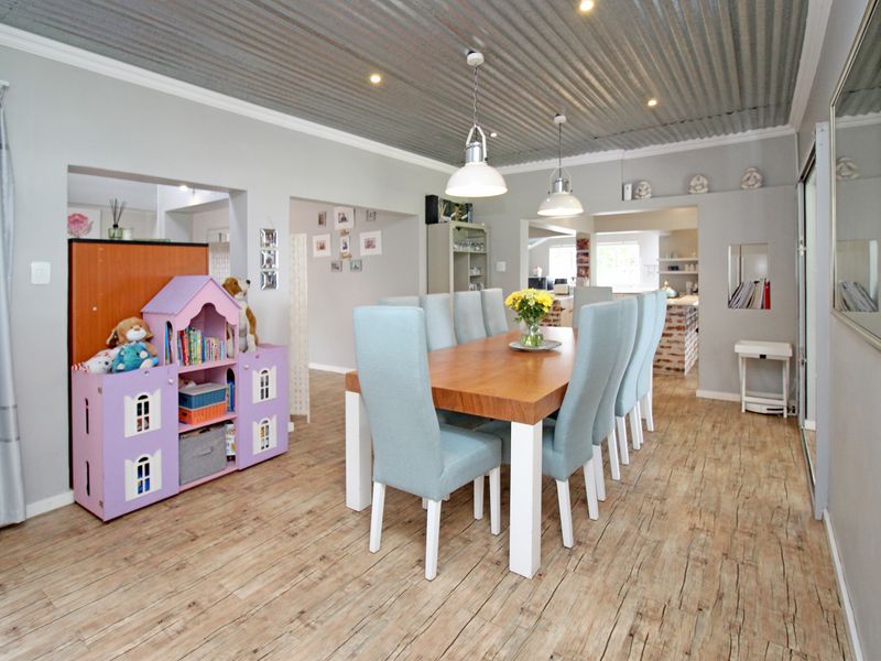 Spacious dining room featuring a unique corrugated metal ceiling, recessed downlights, pendant lighting, and wood-look laminate flooring, creating a modern and inviting atmosphere.
