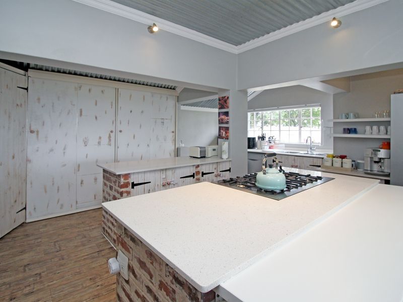 A rustic-style kitchen featuring a central island with a gas cooktop, stone countertops, exposed brick accents, and a corrugated metal ceiling.
