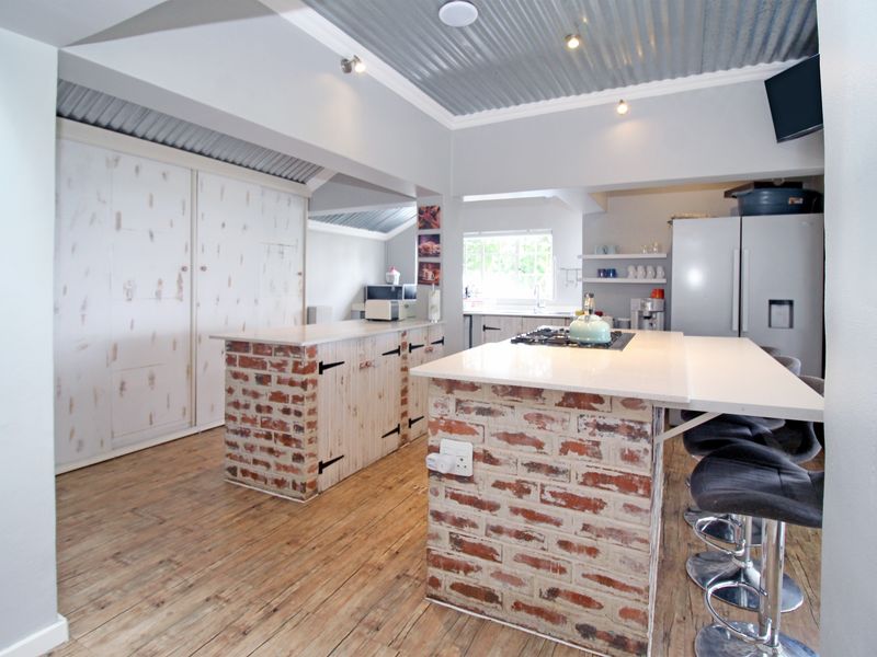 A rustic-style kitchen featuring exposed brick islands with stone countertops, timber flooring, and a distinctive corrugated metal ceiling.