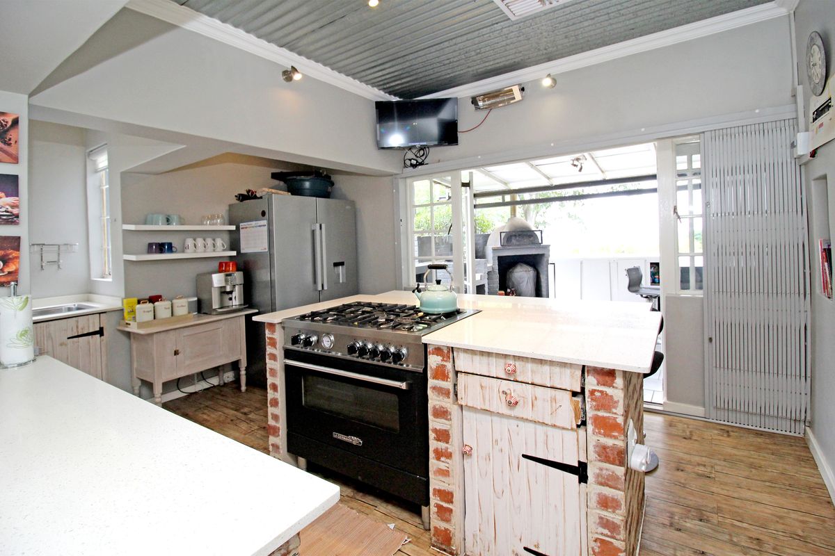 A rustic-style kitchen featuring a central island with a gas stove, stone countertops, exposed brick accents, and a corrugated metal ceiling leading to a patio.