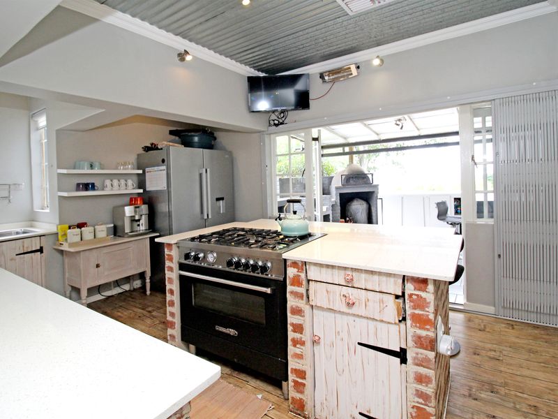 A rustic-style kitchen featuring a central island with a gas stove, stone countertops, exposed brick accents, and a corrugated metal ceiling leading to a patio.