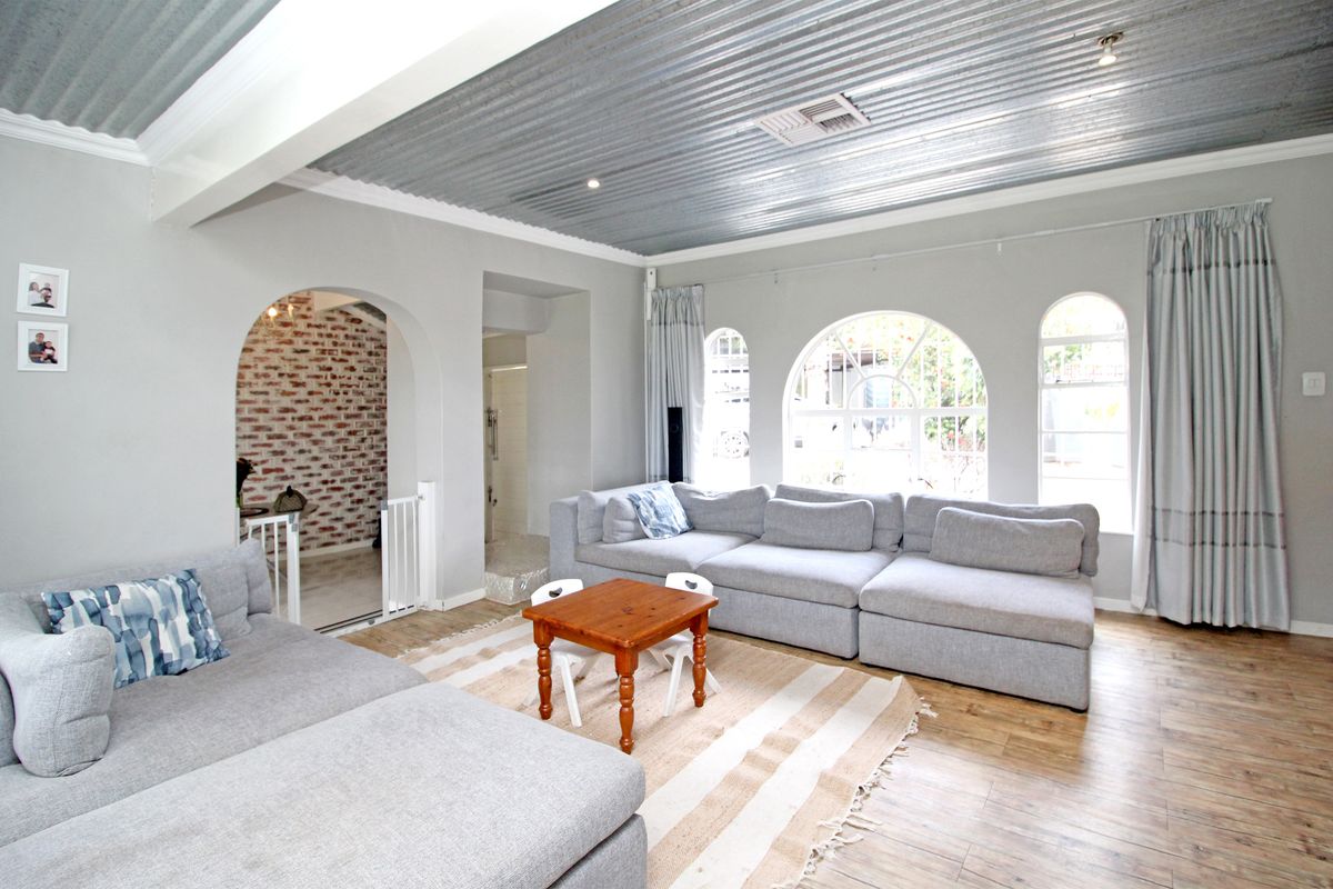 Spacious living room featuring a unique corrugated metal ceiling, arched windows, and an exposed brick feature wall, creating a bright and character-filled living space.