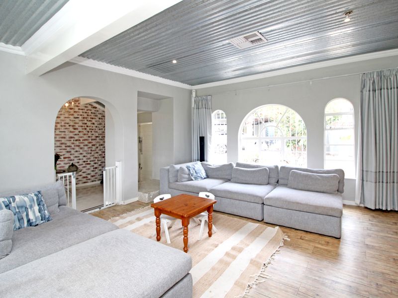 Spacious living room featuring a unique corrugated metal ceiling, arched windows, and an exposed brick feature wall, creating a bright and character-filled living space.