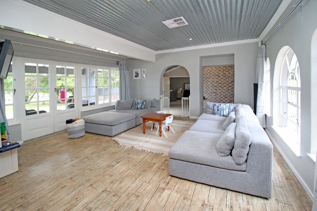 Spacious living room featuring a unique corrugated metal ceiling, timber flooring, arched windows, and an exposed brick accent wall with direct access to the patio.
