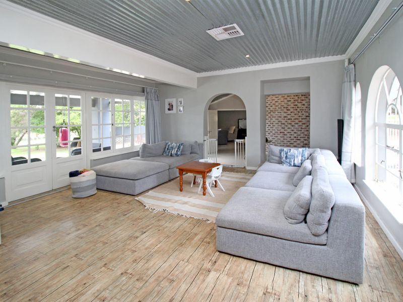 Spacious living room featuring a unique corrugated metal ceiling, timber flooring, arched windows, and an exposed brick accent wall with direct access to the patio.