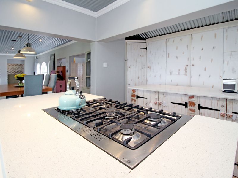 Open plan kitchen featuring a central island with a gas cooktop, stone countertops, and rustic white cabinetry under a corrugated metal ceiling.