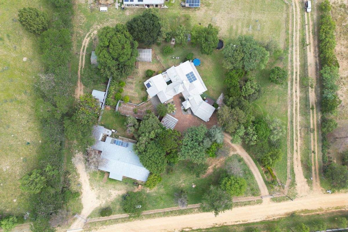 Aerial view of a rural property featuring multiple buildings, solar panel installations, extensive garden areas, and a gravel driveway.