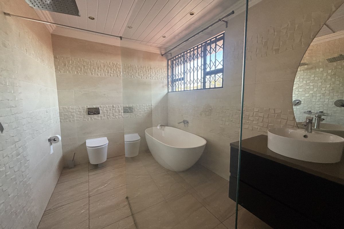 Modern bathroom featuring a freestanding bathtub, wall-mounted toilet, vessel sink with vanity, and a glass-enclosed shower area with neutral tiled finishes.