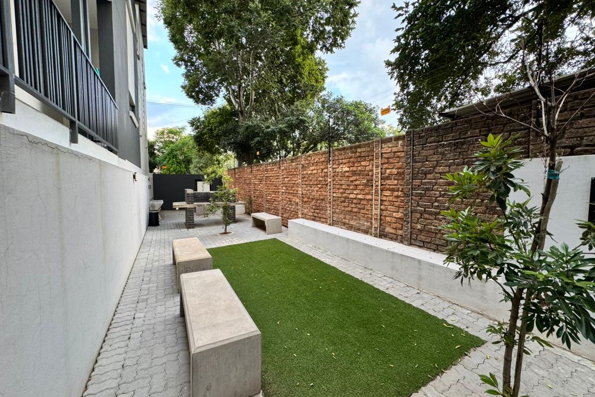 A private rear courtyard featuring a built-in braai, concrete bench seating, artificial lawn, and paved surfaces enclosed by a brick boundary wall.