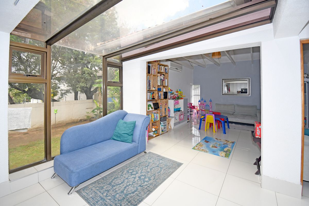 Sun-drenched living area featuring large glass panels, tiled flooring, and an open-plan layout connecting to the garden.
