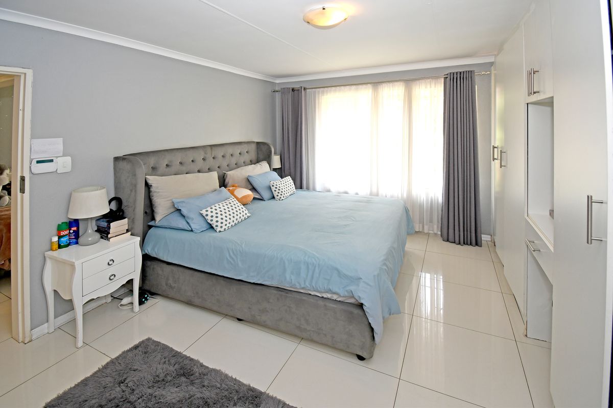A well-maintained bedroom featuring large format floor tiles, built-in cupboards, and a neutral color palette with ample natural light.