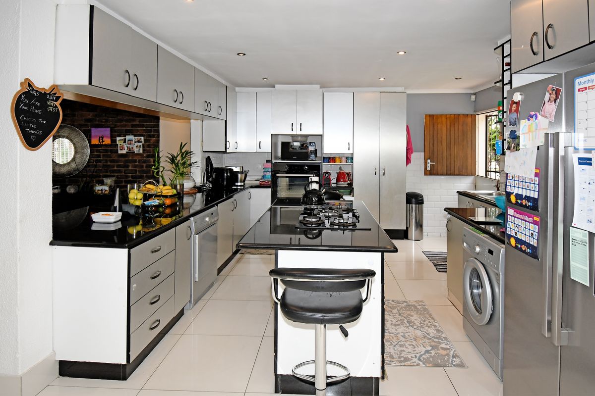 Modern kitchen featuring a central island with gas hob, granite countertops, built-in oven, and ample cabinetry, with integrated laundry space.