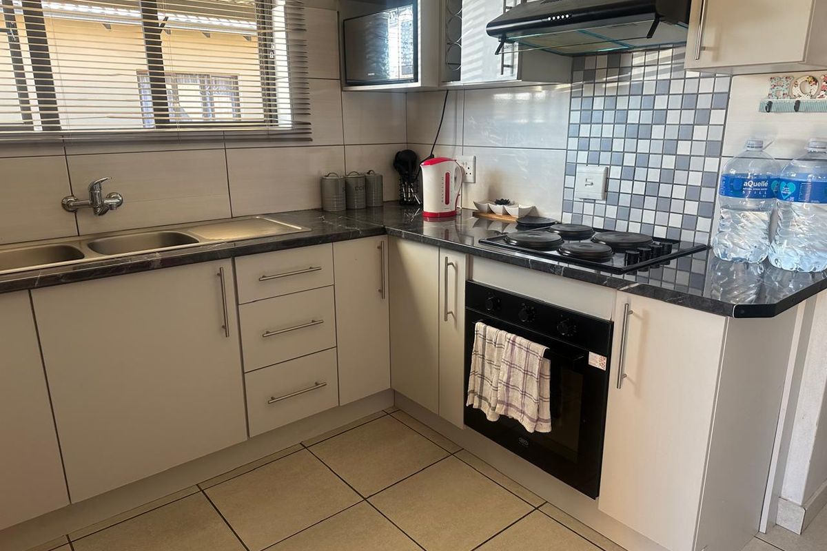 A functional kitchen featuring built-in cabinetry, a double sink, electric hob, oven, and extractor fan with tiled splashbacks and neutral floor tiles.