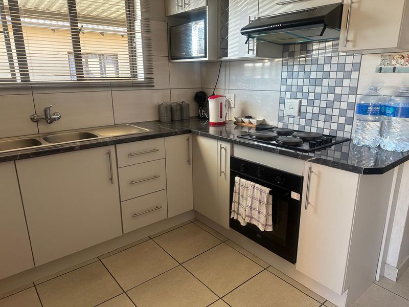 A functional kitchen featuring built-in cabinetry, a double sink, electric hob, oven, and extractor fan with tiled splashbacks and neutral floor tiles.