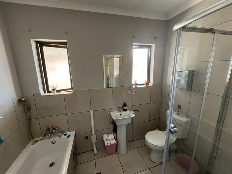 A functional bathroom featuring a pedestal basin, toilet, shower enclosure, and bathtub with neutral wall and floor tiling.