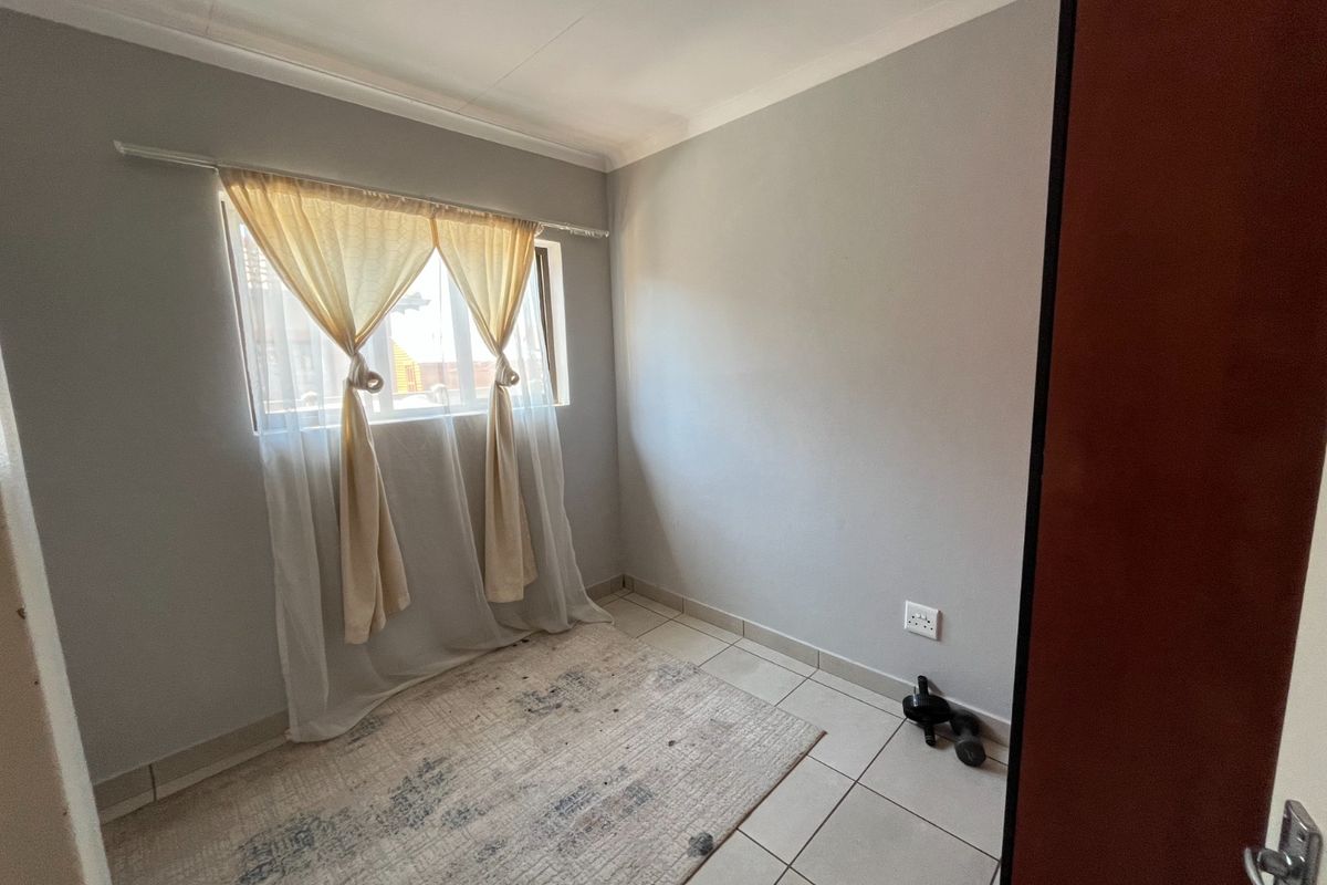 A compact, empty bedroom featuring neutral grey walls, tiled flooring, and a window with natural light, offering a blank canvas for personalization.