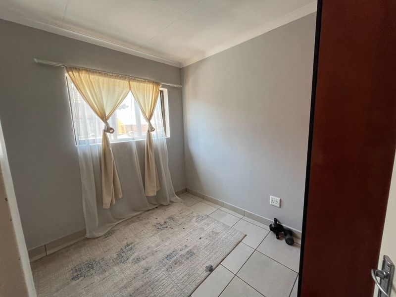 A compact, empty bedroom featuring neutral grey walls, tiled flooring, and a window with natural light, offering a blank canvas for personalization.