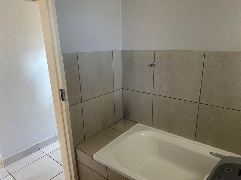 A clean, functional bathroom featuring a built-in bathtub with neutral-toned wall and floor tiling.