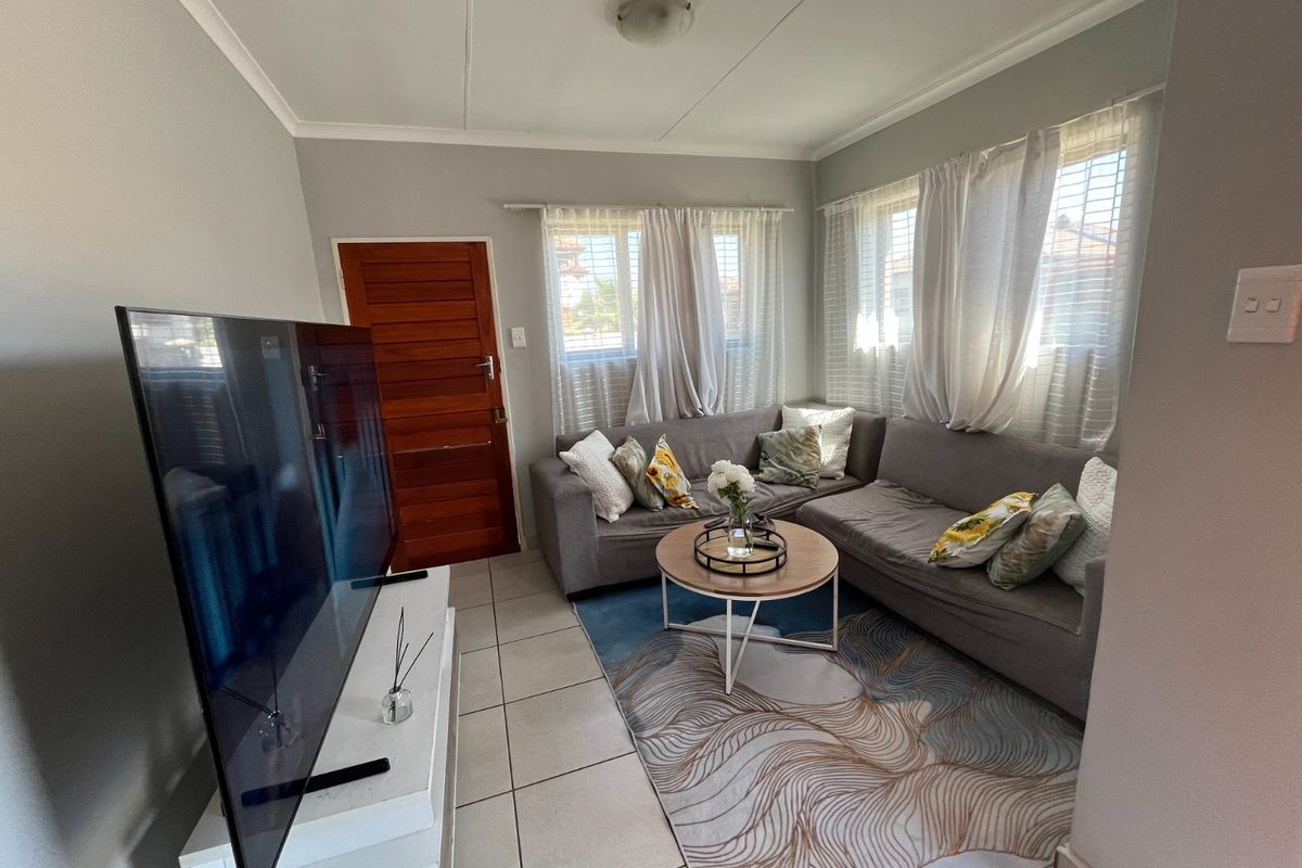 A compact living room featuring tiled flooring, a timber entrance door, and natural light through multiple windows with venetian blinds.