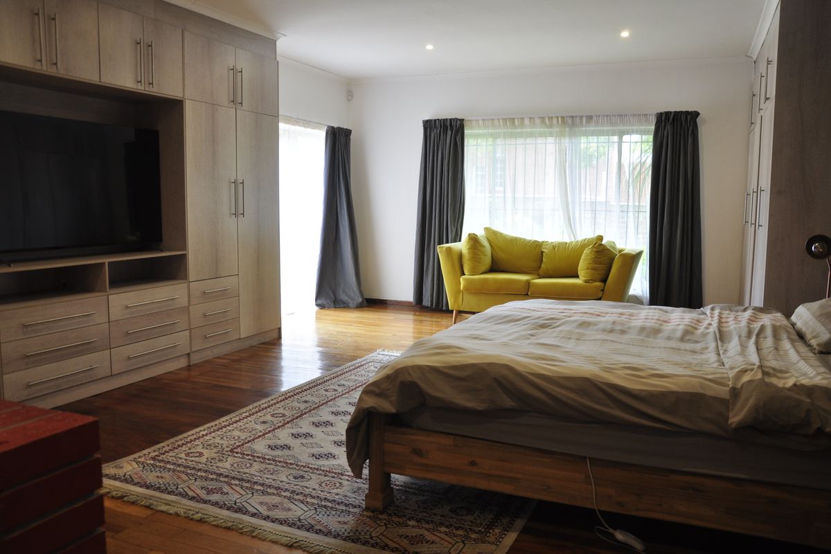 Spacious bedroom featuring extensive built-in cabinetry, warm timber flooring, and large windows allowing for ample natural light.