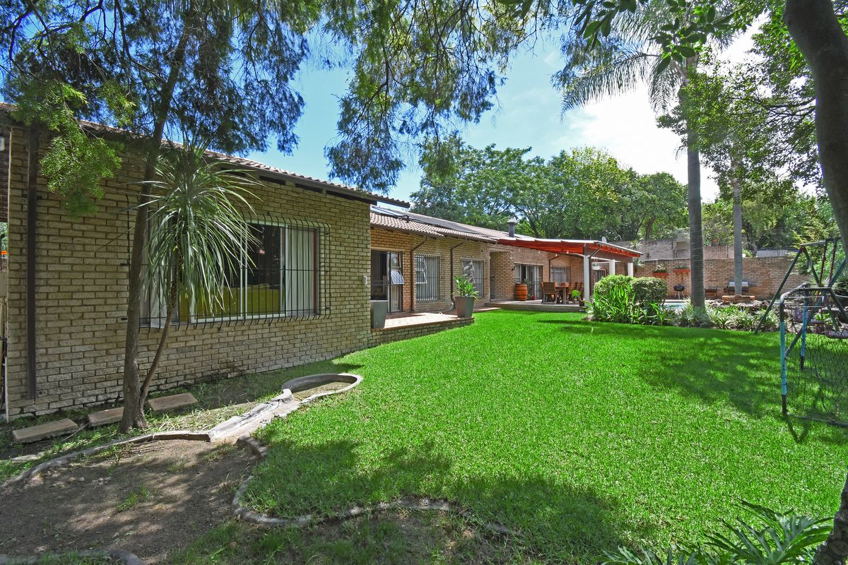 Spacious rear garden featuring a well-maintained lawn, mature trees, and a covered patio area extending from the brick-built house.