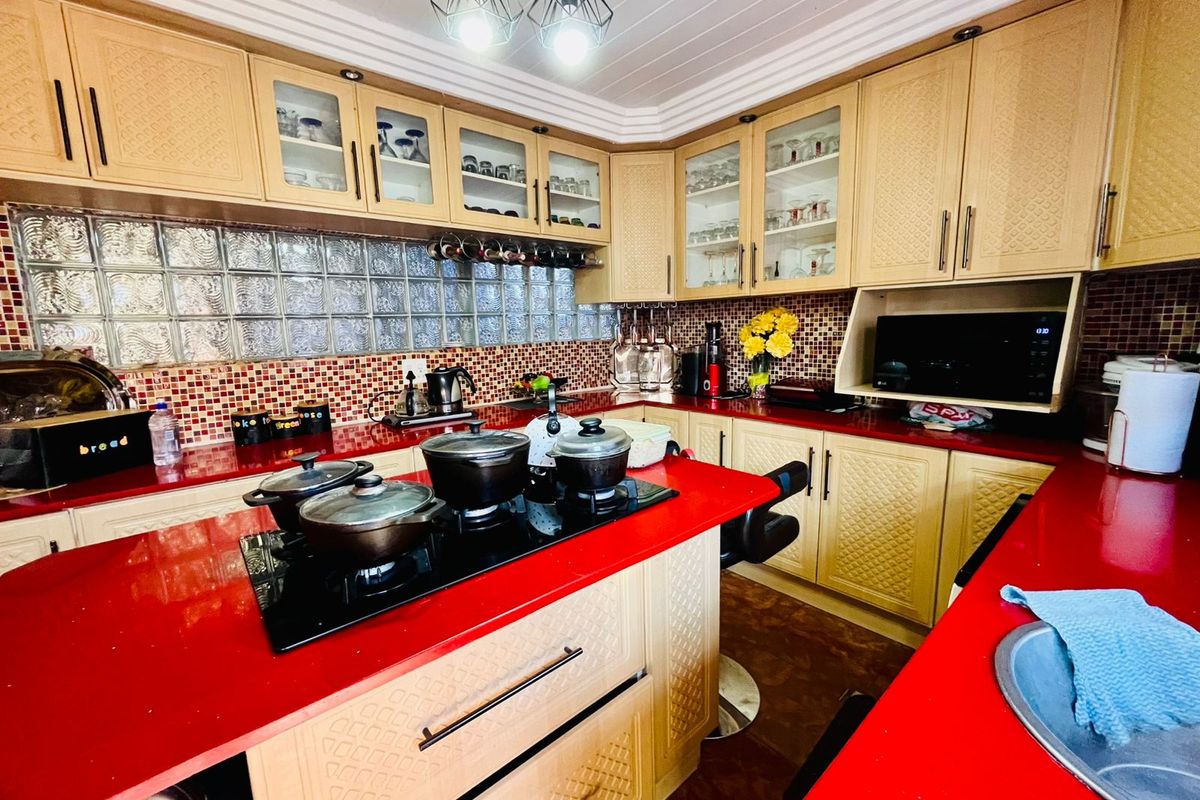 A kitchen featuring light-toned cabinetry, a bold red countertop, a glass block backsplash, and a central island with a built-in cooktop.