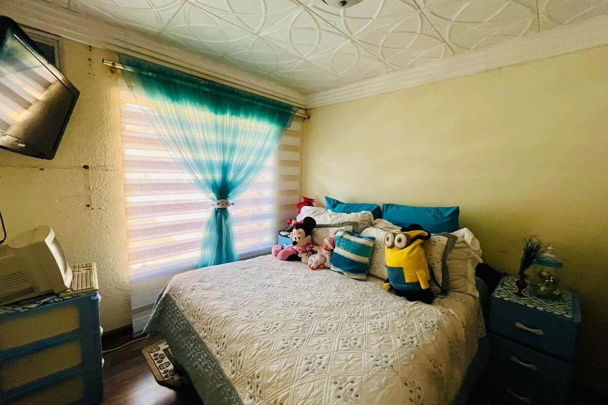 A bedroom featuring a patterned ceiling, laminate flooring, and a window with fitted blinds.